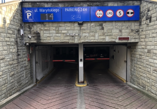 Wjazd na parking podziemny, widoczna tablica z podstawowymi zasadami i aktualną liczbą dostępnych miejsc.