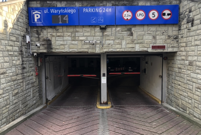 Wjazd na parking podziemny, widoczna tablica z podstawowymi zasadami i aktualną liczbą dostępnych miejsc.