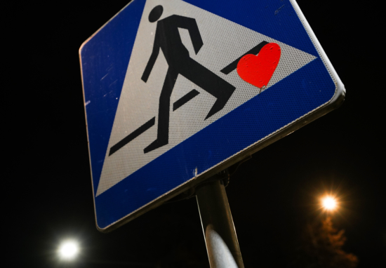 Znak informujący o przejściu dla pieszych, na którym naklejona jest naklejka w kształcie serca.