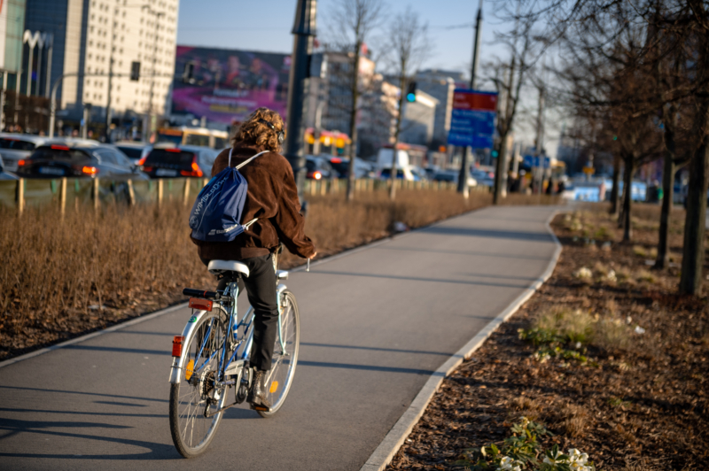 ulica Marszałkowska w rejonie ronda Dmowskiego, na pierwszym planie rowerzystka na nowej asfaltowej drodze dla rowerów biegnącej pośród zieleni