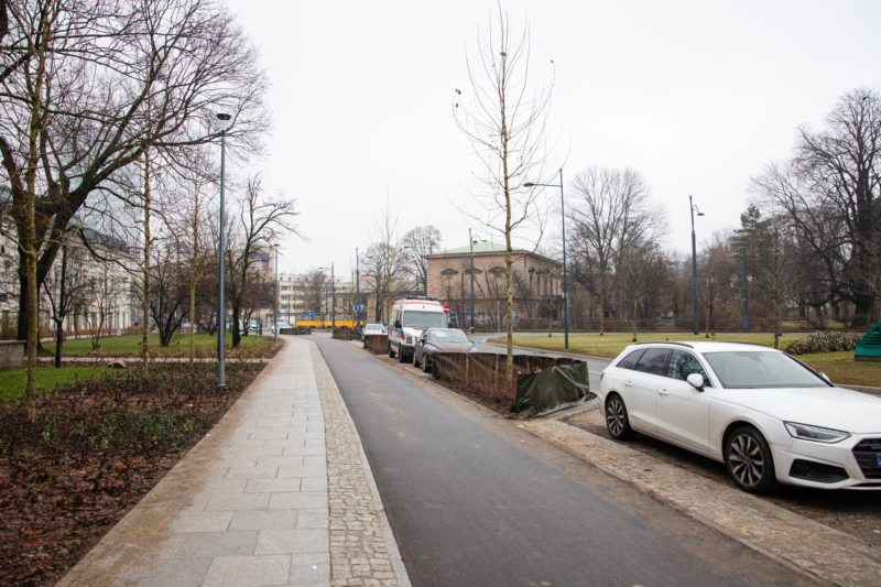 dwa szpalery drzew, pomiędzy nimi nowy granitowy chodnik i asfalowa droga rowerowa, przy jezdni zatoka postojowa, a w niej auta, pomiędzy miejscami parkingowymi również zasadzone drzewa. 