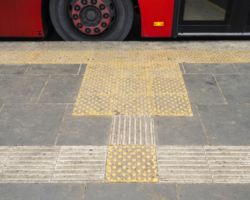 Płyty chodnikowe dla niewidomych przy krawężniku przystanku autobusowego.