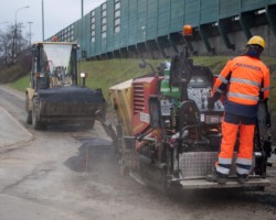 Robotnik rozprowadza masę bitumiczną po drodze rowerowej.