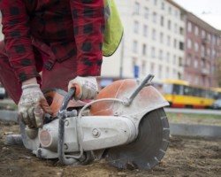 Robotnik podnosi piłę do cięcia płyt chodnikowych.