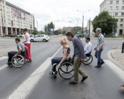 Pracownicy ZDM na wózkach inwalidzkich przejeżdżają przejście dla pieszych.