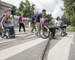 Pracownicy ZDM na wózkach inwalidzkich przejeżdżają przejście z torami tramwajowymi..