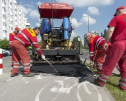 Robotnicy rozprowadzają sproszkowany asflat na ścieżce rowerowej.