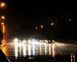 Samochody jadące w nocy ulicą, w trakcie deszczu.