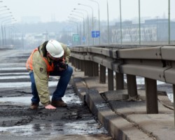 Ekspert dotyka nierówności spalonej nawierzchni mostu.