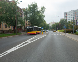 Autobus jedzie ulicą, która jest przedzielona przejściem z azylami