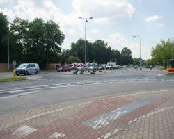 Na zdjęciu widać chodnik, rondo, samochód policyjny, autobus i inne auta