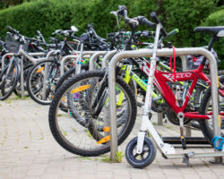 Zdjęcie przedstawia parking rowerowy ze stojakami typu odwrócone "U". Na parkingu licznie stoją rowery, a na pierwszym planie jest hulajnoga.