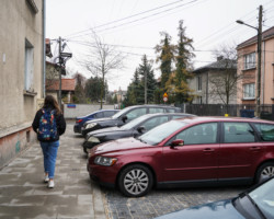 Spacerująca osoba i zaparkowane samochody.