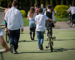 Młodzi ludzie idą, osoba w białej koszuli prowadzi rower