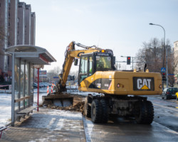 Żółta koparka Caterpillar likwiduje stary chodnik przy przystanku