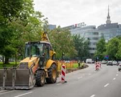 Roboty drogowe trwają. Ulicą przejeżdża żółta koparka, a pracownicy przekopują krawędzie jezdni. Ruch jest częściowo ograniczony