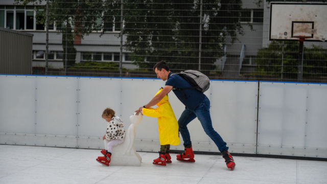 Mężczyzna jedzie na łyżwach z dwójką dzieci po syntetycznym lodowisku