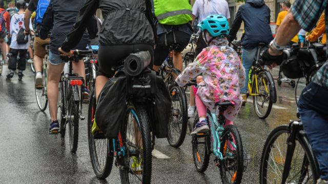 Tłum ludzi jadący na rowerach mokrą od deszczu ulicą