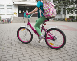 Uczennica jadąca na rowerze z plecakiem, w tle szkoła