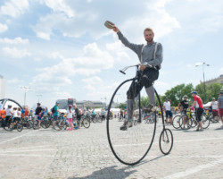 Rowerzysta na retro rowerze z dużym przednim kołem pozdrawia zdejmując czapkę