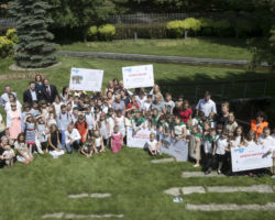 Zwycięscy uczniowie siedzą na trawniku w dużej grupie, podnosząc tablice wyróżniające