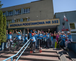 Uczniowie SP 352 na tle swojej szkoły wraz ze sprzętami - rowerami, hulajnogami